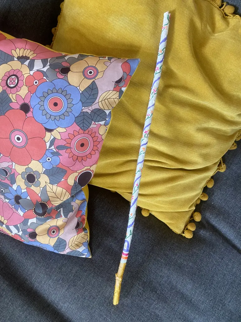 Bâton de parole Magie, long et blanc avec une frise de fleurs rose et orange fluo + une rayure mauve en colimaçon tout le long du bâton.