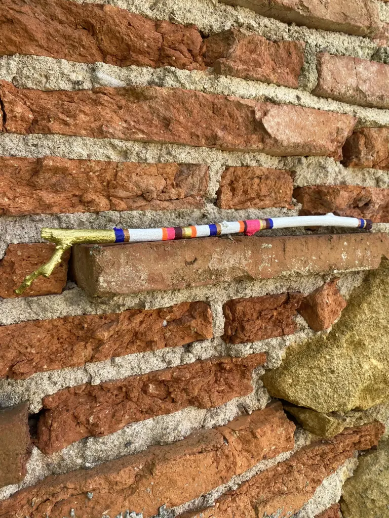 baton Edit - blanc avec des couleurs fluos, du marron, du cuivré, de l'or et du bleu profond- posé à l'orizontal avec en fond un mur de brique