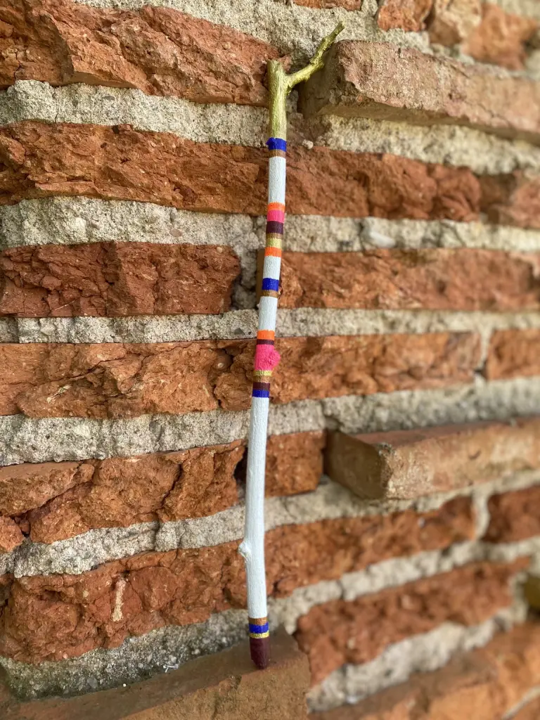 fond en brique - baton blanc avec bandes de couleurs rose-orange-marron-cuivre-doré et bleu profondposé à la verticale - f