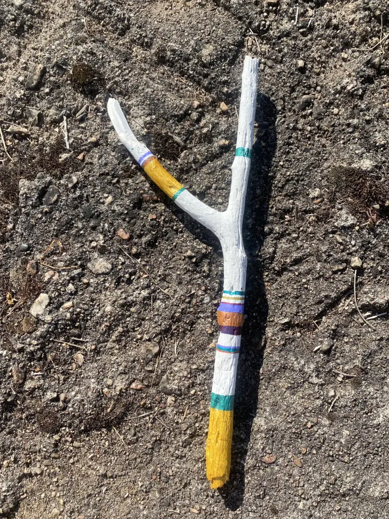 baton de parole 51 cm blanc avec teintes metallisées or, cuivre, vert émeraude. teintes mates mauves, prunes, bleu et chocolat. Fond sol de terrasse brut avec aspérités
